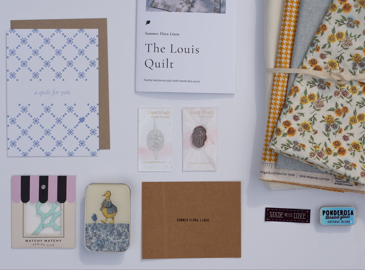 A quilted fabric bundle with floral and gingham patterns tied with a string, displayed alongside a quilt pattern booklet, cards, and a brown envelope on a light gray background.